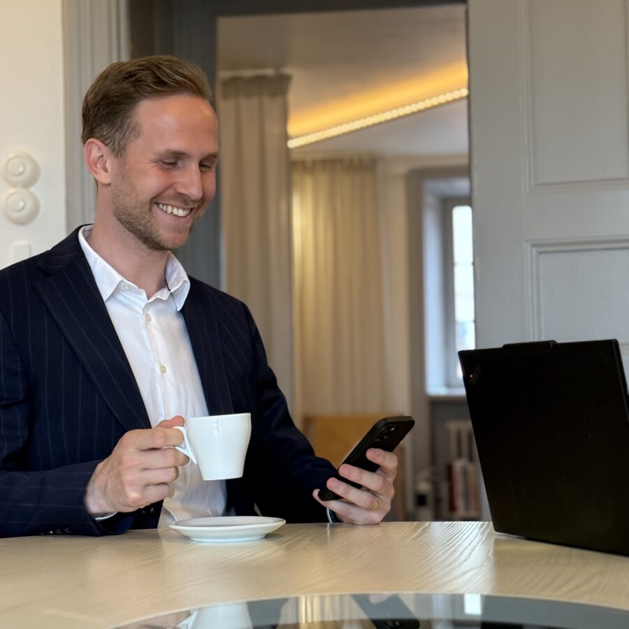man smiling looking at phone with a coffee cup in one hand